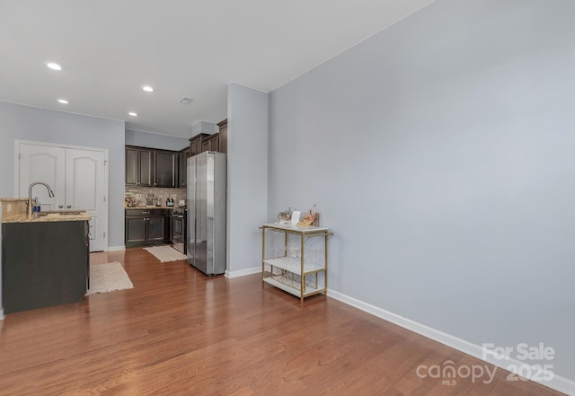 kitchen featuring dark brown cabinetry, decorative backsplash, dark wood-style flooring, freestanding refrigerator, and a sink