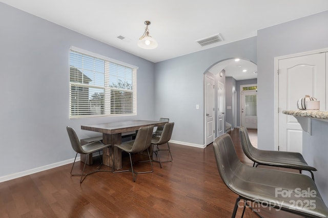 dining space featuring dark wood-style floors, baseboards, visible vents, and arched walkways