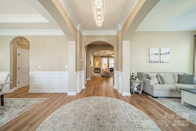 entrance foyer featuring arched walkways, ornamental molding, a wainscoted wall, and wood finished floors