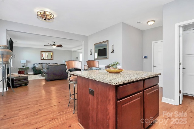 kitchen featuring light stone counters, a breakfast bar, light wood-style flooring, open floor plan, and a kitchen island