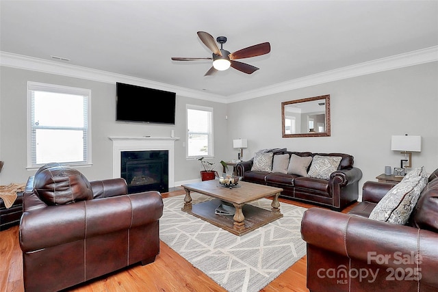 living room with a fireplace with flush hearth, visible vents, wood finished floors, and ornamental molding