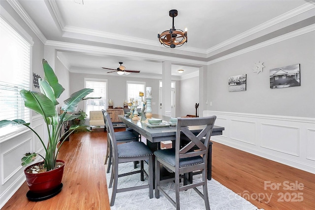 dining space with a wainscoted wall, ornamental molding, wood finished floors, and a decorative wall