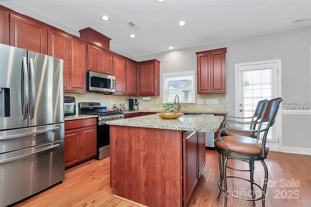 kitchen with light wood finished floors, appliances with stainless steel finishes, a kitchen island, and visible vents