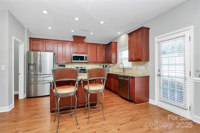 kitchen featuring a kitchen island, a sink, stainless steel appliances, light wood-style floors, and backsplash