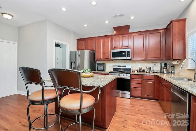 kitchen with a center island, appliances with stainless steel finishes, light wood-style floors, a sink, and light stone countertops