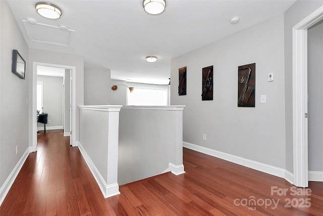 corridor featuring baseboards, dark wood-type flooring, an upstairs landing, and attic access