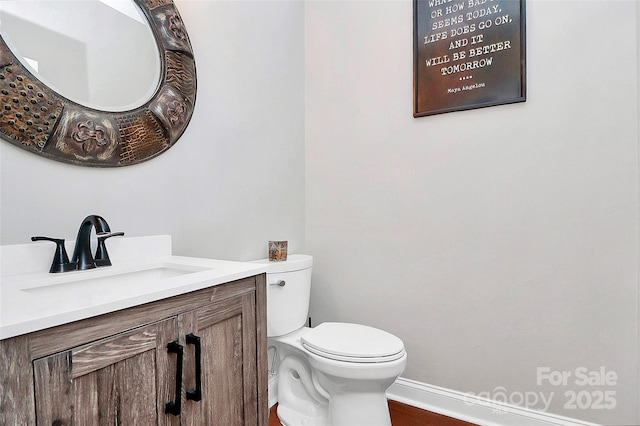 half bathroom with toilet, baseboards, and vanity