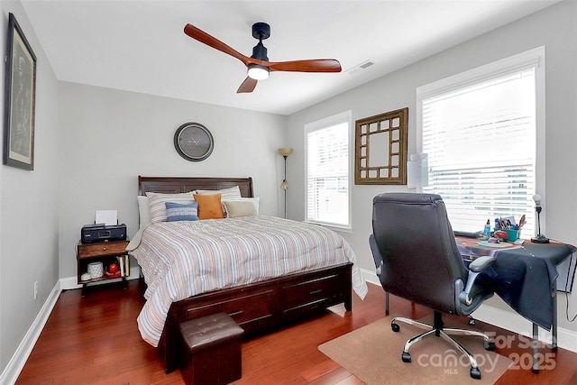 bedroom with a ceiling fan, visible vents, baseboards, and wood finished floors