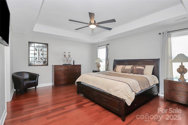 bedroom featuring visible vents, multiple windows, a tray ceiling, and dark wood finished floors