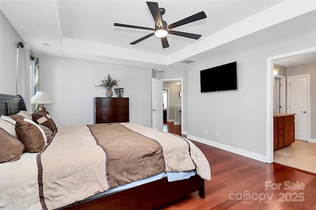 bedroom featuring connected bathroom, wood finished floors, visible vents, baseboards, and a raised ceiling