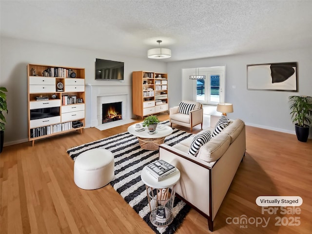 living room with a textured ceiling, a fireplace with flush hearth, wood finished floors, and baseboards