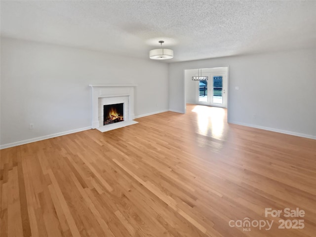 unfurnished living room featuring french doors, a brick fireplace, a textured ceiling, light wood-type flooring, and baseboards