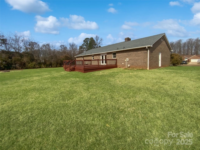 rear view of house featuring a chimney, a deck, a lawn, and brick siding