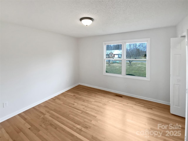 empty room with visible vents, baseboards, a textured ceiling, and light wood finished floors