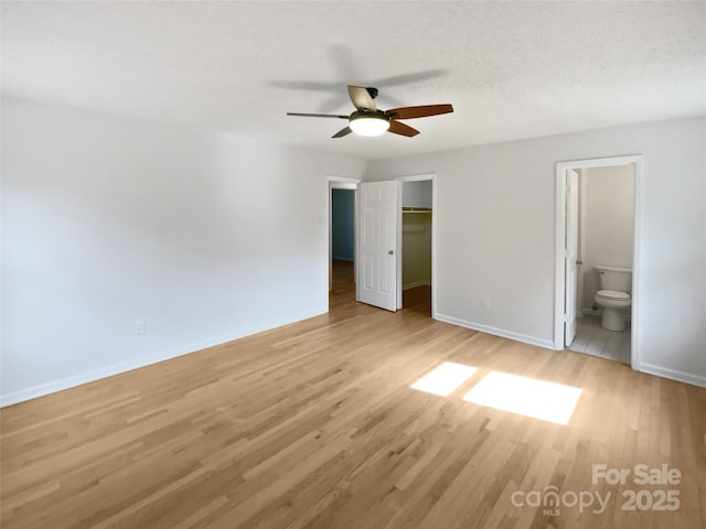 unfurnished bedroom with ensuite bathroom, baseboards, a spacious closet, a closet, and light wood finished floors