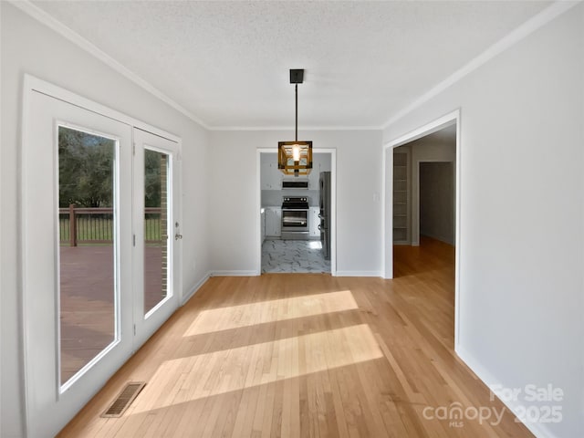 unfurnished dining area with visible vents, light wood-style floors, ornamental molding, a textured ceiling, and baseboards