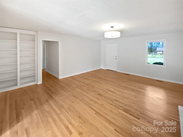 spare room with a textured ceiling, light wood finished floors, built in features, and baseboards