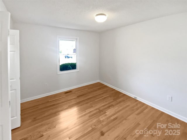 unfurnished room featuring light wood-type flooring, visible vents, a textured ceiling, and baseboards