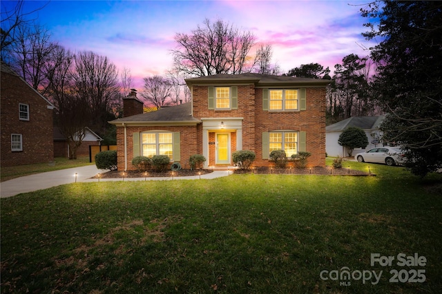 view of front of property featuring concrete driveway, brick siding, a chimney, and a front yard