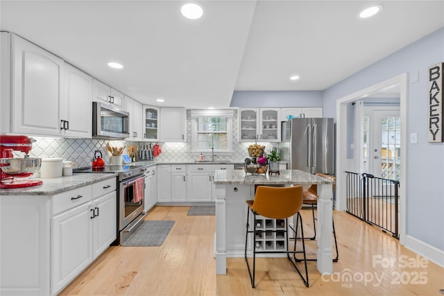 kitchen featuring glass insert cabinets, light wood-style floors, a kitchen bar, and appliances with stainless steel finishes