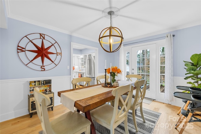 dining room featuring light wood-type flooring, a chandelier, crown molding, and wainscoting