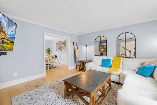 living room featuring light wood-style floors, stairway, baseboards, and crown molding