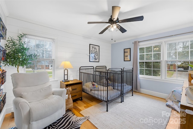 bedroom featuring a nursery area, multiple windows, crown molding, and light wood-style flooring