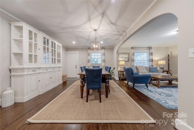 dining area with arched walkways, a notable chandelier, dark wood finished floors, and ornamental molding