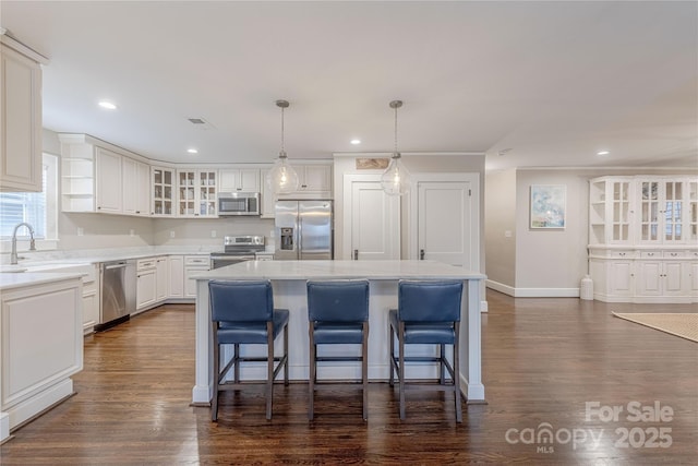 kitchen with a kitchen bar, a kitchen island, stainless steel appliances, white cabinets, and dark wood-style flooring