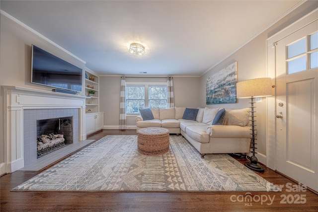 living room featuring crown molding, wood finished floors, baseboards, and a tile fireplace