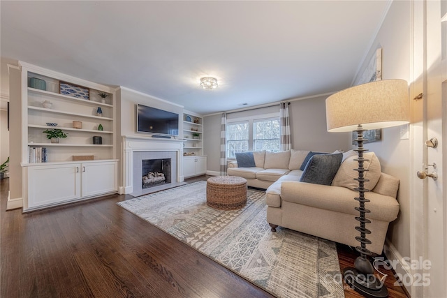 living area with baseboards, a fireplace with flush hearth, dark wood finished floors, and crown molding