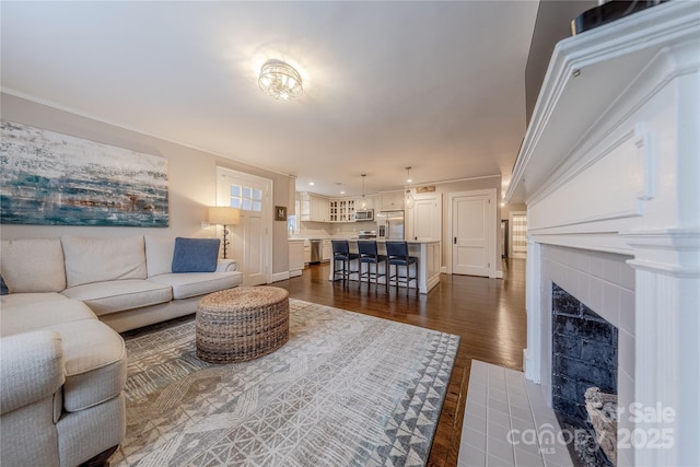 living area with dark wood finished floors, a fireplace with flush hearth, baseboards, and ornamental molding