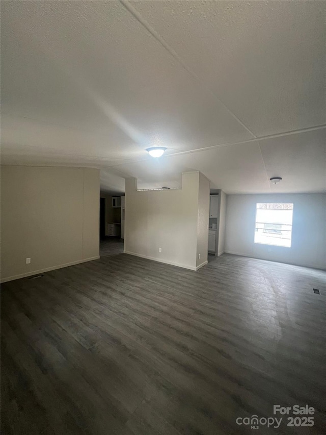 empty room with visible vents, a textured ceiling, baseboards, and dark wood-type flooring