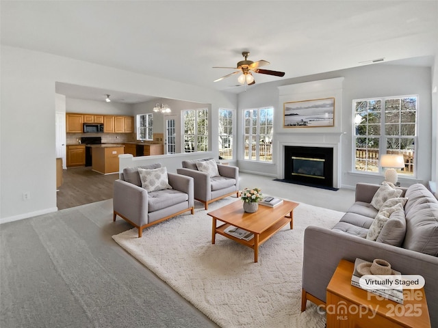 living room with a fireplace with flush hearth, plenty of natural light, baseboards, and ceiling fan with notable chandelier