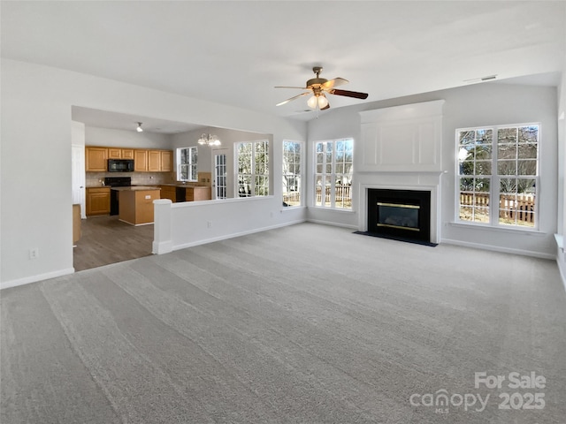 unfurnished living room with visible vents, baseboards, a fireplace with flush hearth, carpet flooring, and ceiling fan with notable chandelier