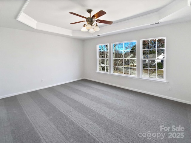 spare room featuring dark colored carpet, a tray ceiling, visible vents, and baseboards