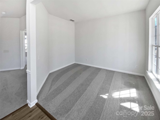 carpeted spare room featuring wood finished floors, visible vents, and baseboards