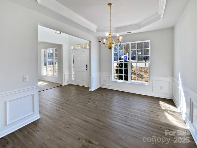 unfurnished dining area featuring dark wood-style floors, a tray ceiling, a wainscoted wall, and an inviting chandelier