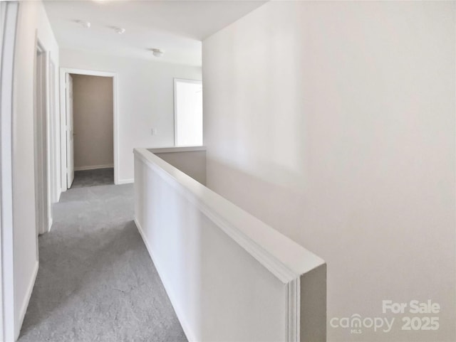 hall featuring carpet floors, baseboards, and an upstairs landing