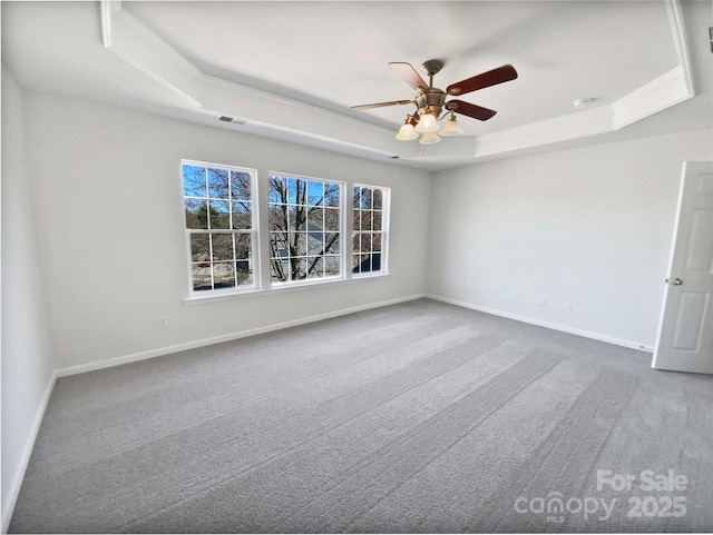 empty room with carpet floors, a tray ceiling, visible vents, and baseboards