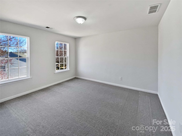 spare room featuring baseboards, visible vents, and dark carpet