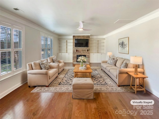 living room featuring ceiling fan, ornamental molding, a fireplace, and wood finished floors