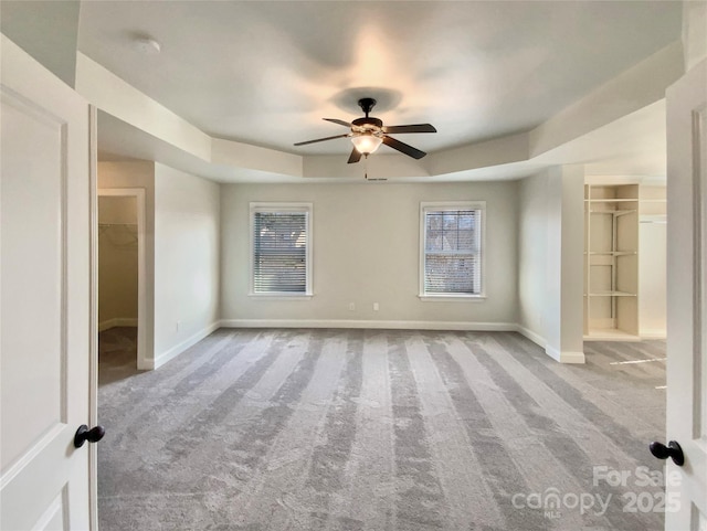 spare room with a ceiling fan, a raised ceiling, carpet flooring, and baseboards