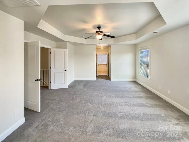 empty room with carpet flooring, a raised ceiling, and baseboards