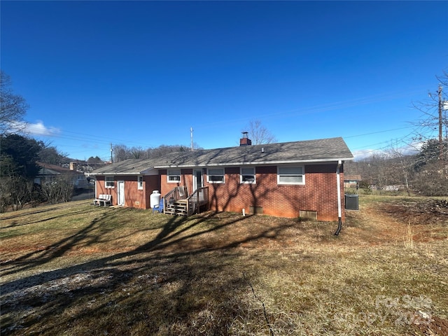 rear view of house featuring central air condition unit, a yard, a chimney, and brick siding