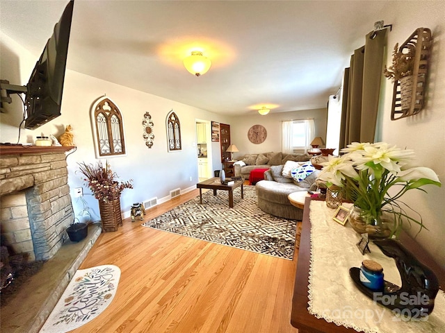 living area featuring visible vents, baseboards, a fireplace with raised hearth, and wood finished floors