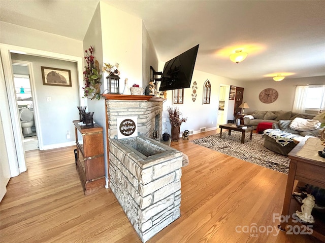 living room with baseboards, a fireplace, visible vents, and light wood finished floors