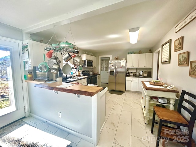 kitchen featuring a breakfast bar area, stainless steel appliances, a peninsula, white cabinetry, and marble finish floor