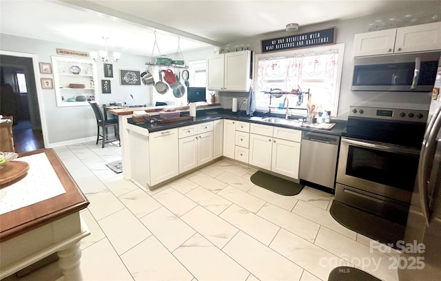 kitchen with marble finish floor, dark countertops, appliances with stainless steel finishes, a sink, and a peninsula