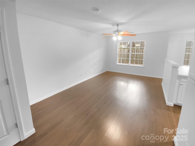 empty room with ceiling fan, wood finished floors, and baseboards